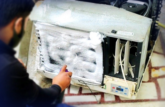A man is servicing a heavily frosted window AC.
